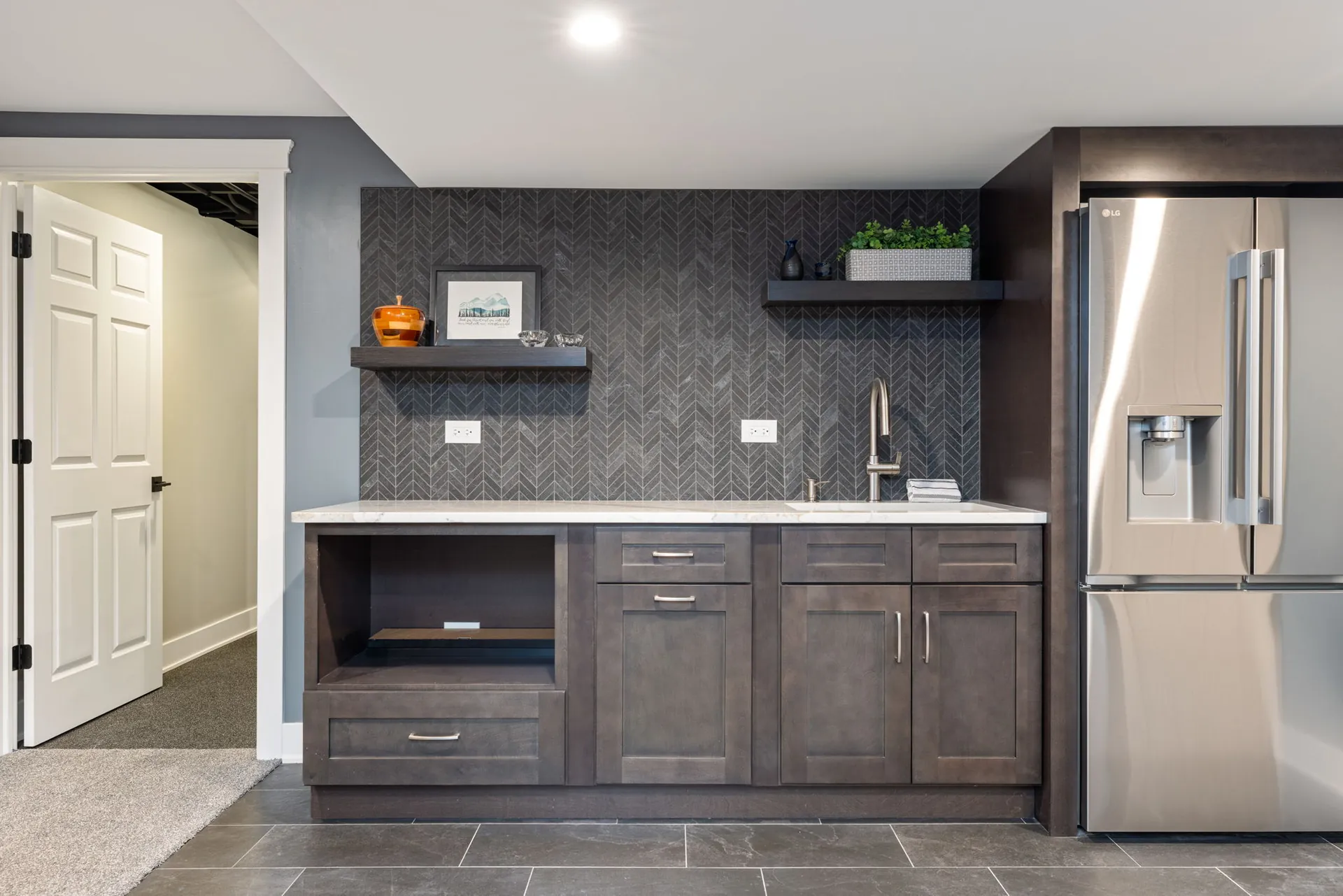 Finished basement wet bar with floating shelves and full-size refrigerator