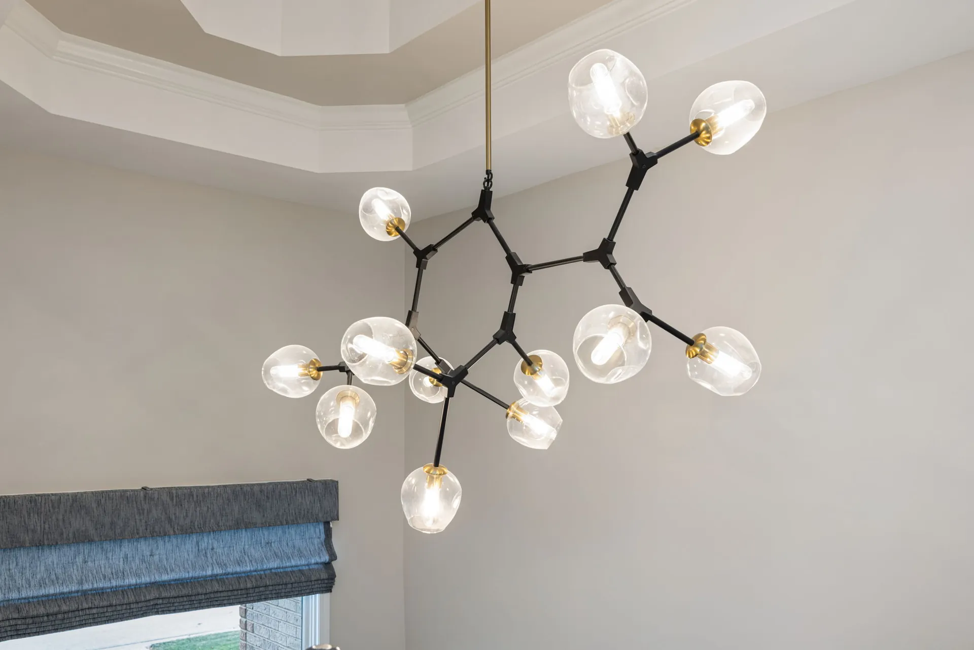 Black and brass glass globe chandelier under a tray ceiling