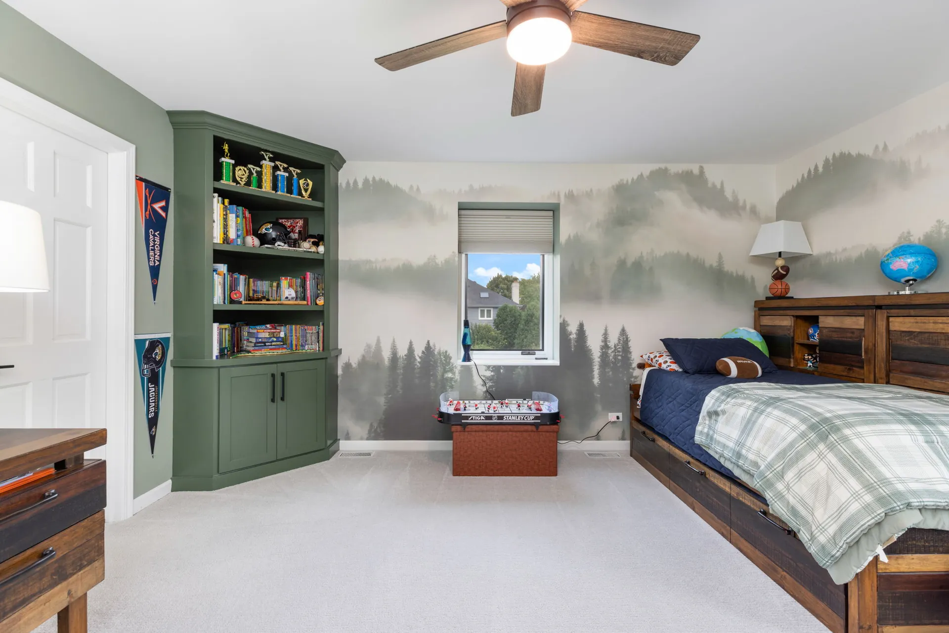 Green built-in bookcase against forest mural wallpaper